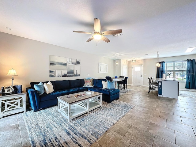 living area featuring ceiling fan, stone finish floor, visible vents, and baseboards