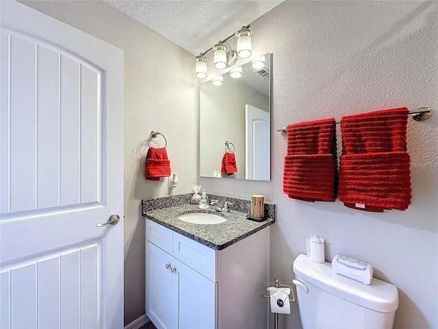 bathroom featuring a textured wall, vanity, toilet, and a textured ceiling