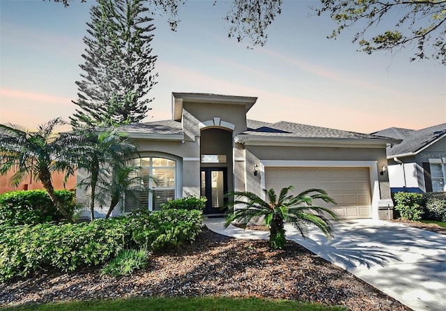 prairie-style home featuring a garage, driveway, a shingled roof, and stucco siding