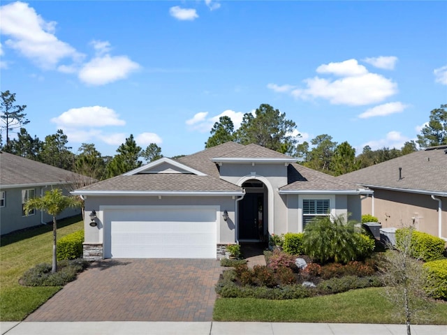 single story home featuring an attached garage, roof with shingles, decorative driveway, and stucco siding