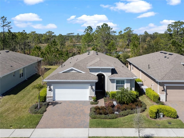 ranch-style house with decorative driveway, stucco siding, a shingled roof, a front yard, and a garage