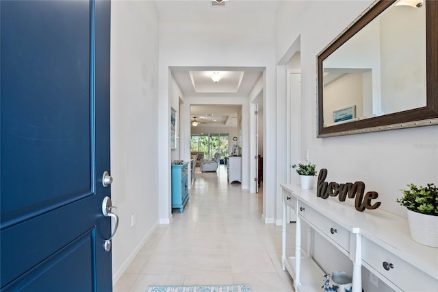 entryway featuring light tile patterned floors, a tray ceiling, and baseboards