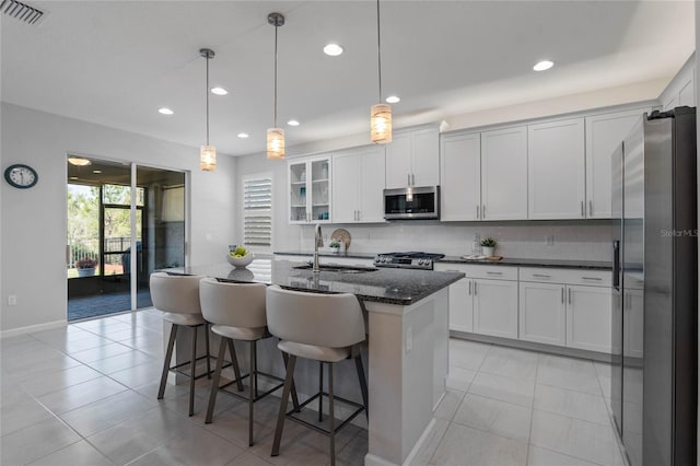 kitchen with stainless steel appliances, a breakfast bar, visible vents, decorative backsplash, and dark stone counters