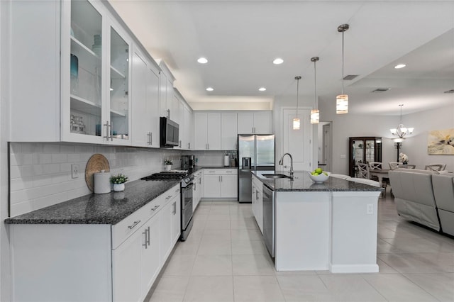 kitchen with decorative backsplash, appliances with stainless steel finishes, open floor plan, a sink, and dark stone counters