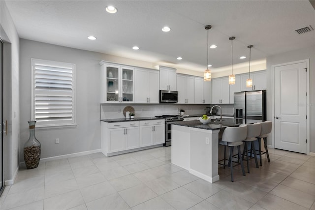 kitchen featuring tasteful backsplash, visible vents, a kitchen breakfast bar, a kitchen island with sink, and stainless steel appliances