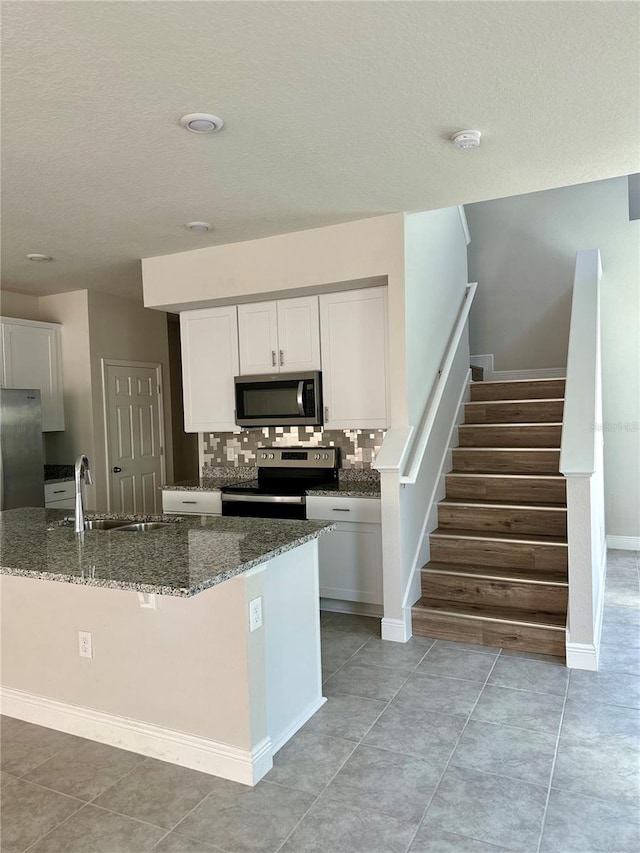 kitchen featuring stainless steel appliances, dark stone countertops, backsplash, and white cabinets