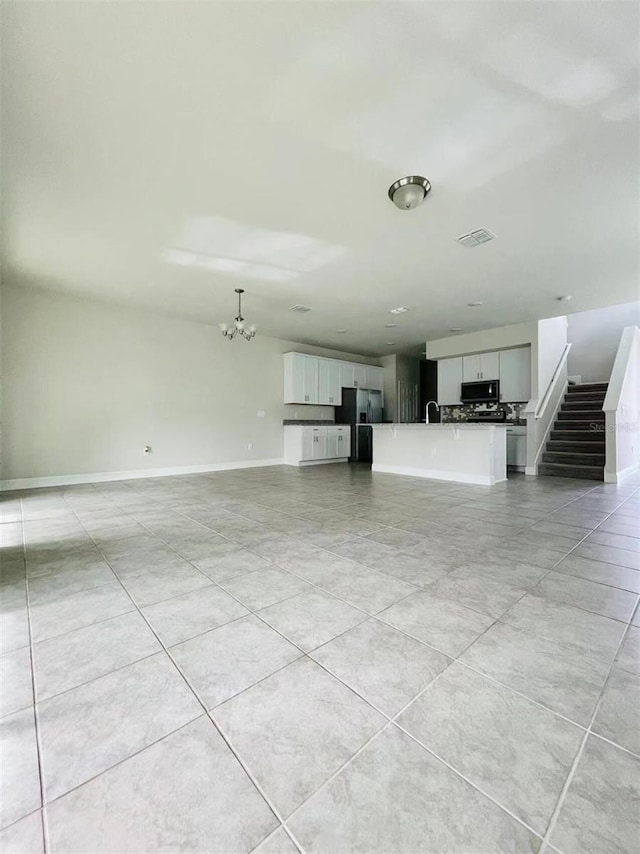 unfurnished living room featuring a notable chandelier, a sink, visible vents, baseboards, and stairway