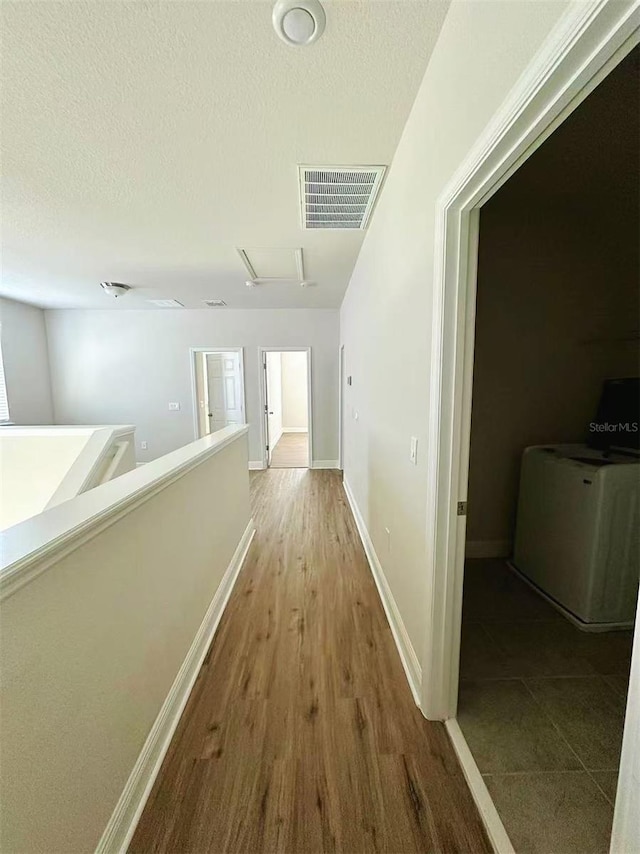 hallway featuring washer / dryer, baseboards, visible vents, a textured ceiling, and an upstairs landing