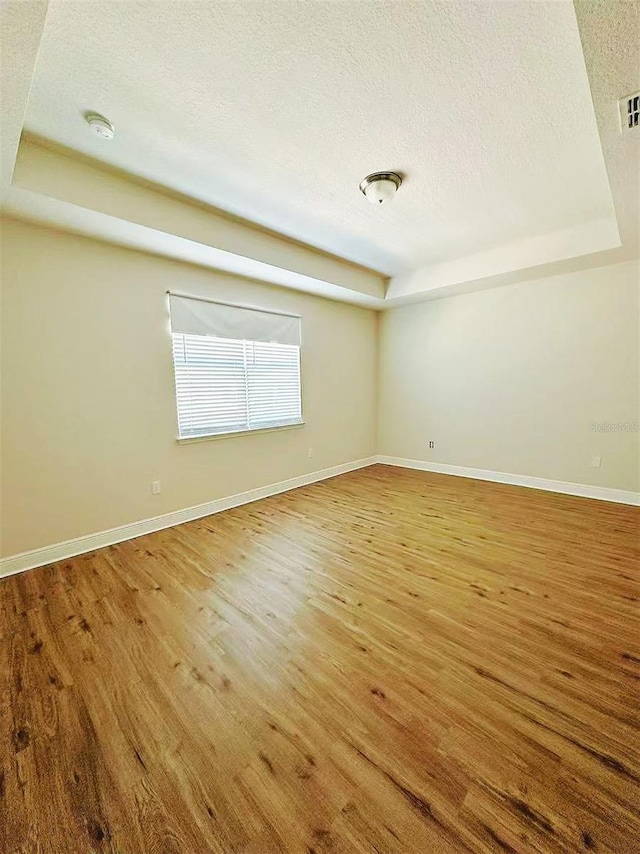 empty room with a tray ceiling, a textured ceiling, and wood finished floors