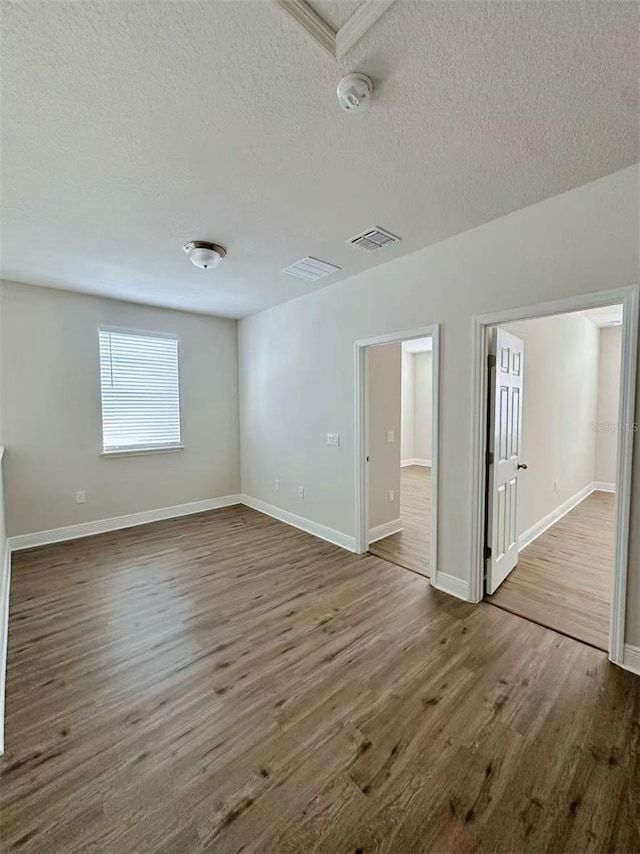 empty room featuring a textured ceiling, wood finished floors, visible vents, and baseboards