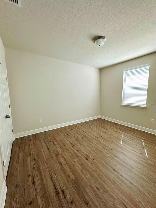 unfurnished bedroom featuring a textured ceiling, baseboards, and dark wood-type flooring