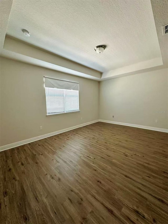 spare room featuring baseboards, a raised ceiling, and dark wood-style flooring