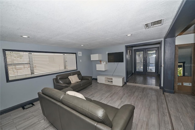 living area featuring french doors, visible vents, wood tiled floor, a textured ceiling, and baseboards