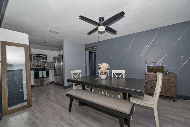 dining space featuring a textured ceiling, wood finish floors, visible vents, and a ceiling fan