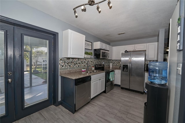 kitchen with decorative backsplash, appliances with stainless steel finishes, wood tiled floor, white cabinetry, and a sink