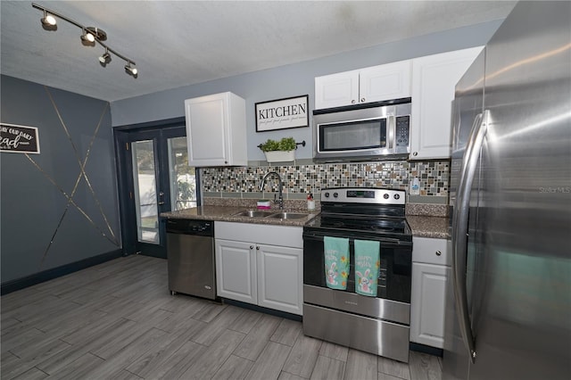 kitchen featuring stainless steel appliances, wood finish floors, a sink, white cabinets, and decorative backsplash