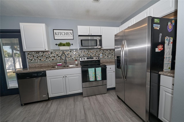 kitchen with tasteful backsplash, white cabinets, wood tiled floor, stainless steel appliances, and a sink