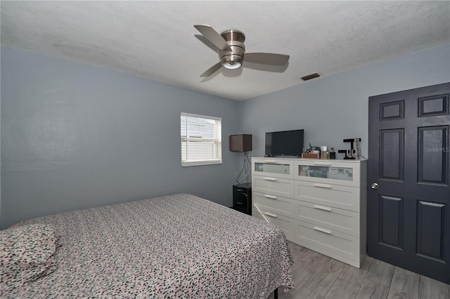 bedroom featuring visible vents, ceiling fan, light wood-style flooring, and a textured ceiling