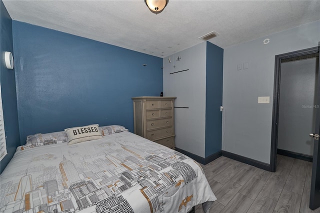 bedroom featuring visible vents, a textured ceiling, baseboards, and wood finished floors