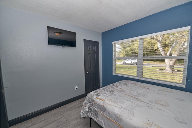 bedroom featuring a textured ceiling, baseboards, and wood finished floors