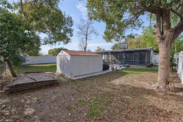 view of yard with a sunroom, a fenced backyard, a storage shed, and an outbuilding