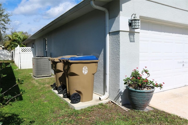 view of side of home with an attached garage, fence, central AC, and stucco siding