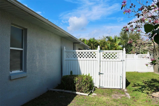 exterior space featuring a gate, fence, a lawn, and stucco siding