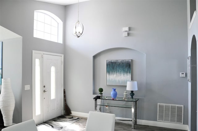 foyer entrance with baseboards, a high ceiling, visible vents, and a chandelier