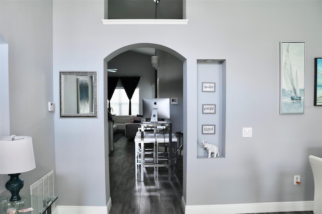 corridor with arched walkways, visible vents, baseboards, and wood finished floors