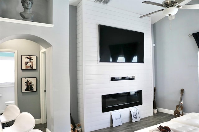 living room with arched walkways, dark wood-type flooring, a ceiling fan, visible vents, and baseboards