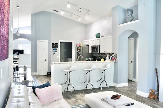 kitchen featuring arched walkways, a breakfast bar area, appliances with stainless steel finishes, high vaulted ceiling, and a peninsula