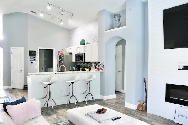 kitchen featuring arched walkways, high vaulted ceiling, appliances with stainless steel finishes, and a kitchen breakfast bar