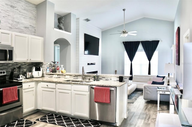 kitchen with appliances with stainless steel finishes, open floor plan, white cabinetry, a sink, and a peninsula