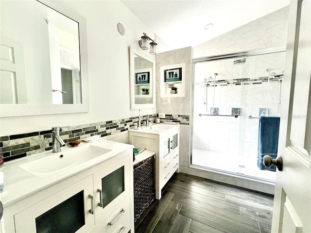 full bath with lofted ceiling, a sink, two vanities, a shower stall, and tasteful backsplash