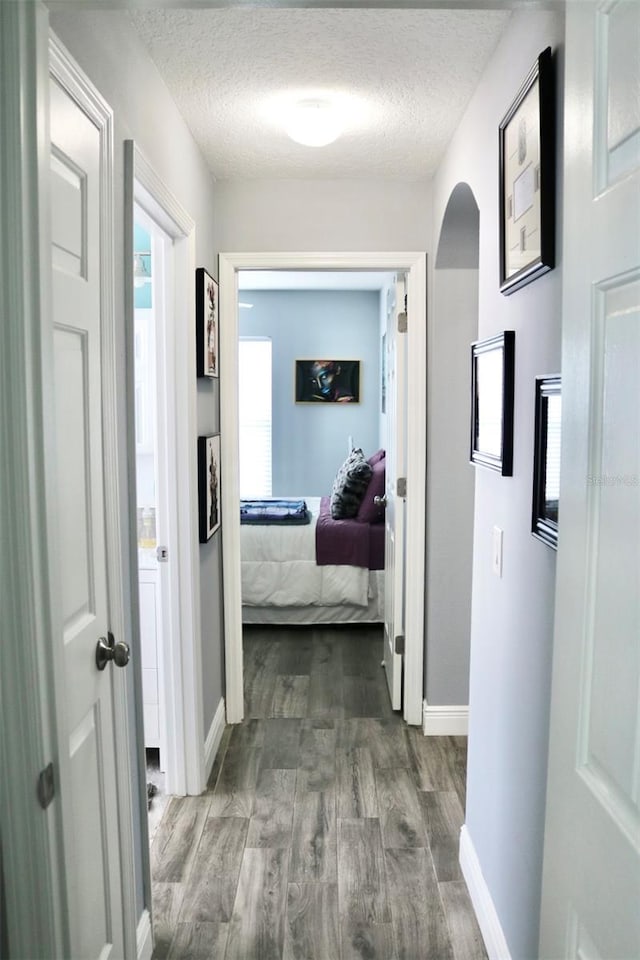 hallway with arched walkways, dark wood finished floors, a textured ceiling, and baseboards