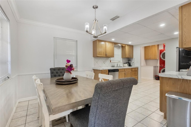 dining area featuring light tile patterned floors, visible vents, ornamental molding, stacked washing maching and dryer, and a chandelier