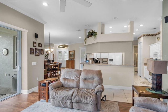 living room featuring light wood-type flooring, recessed lighting, baseboards, and ceiling fan with notable chandelier