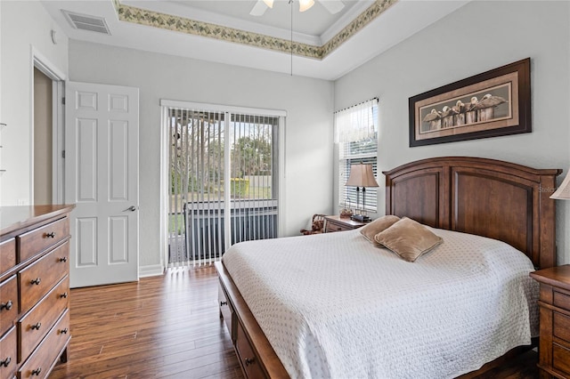 bedroom with a tray ceiling, visible vents, dark wood-type flooring, a ceiling fan, and access to outside