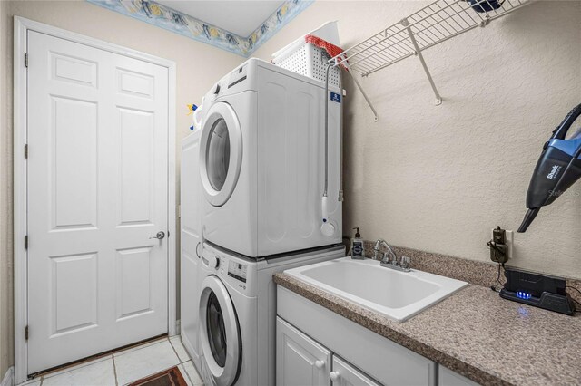 washroom with light tile patterned floors, cabinet space, a textured wall, stacked washer / drying machine, and a sink