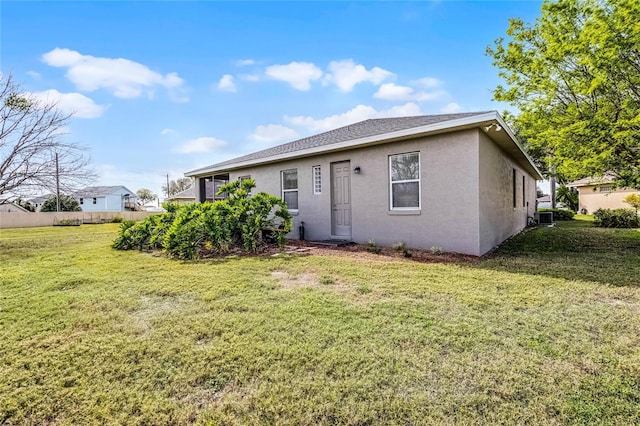 back of property with a shingled roof, cooling unit, a lawn, and stucco siding