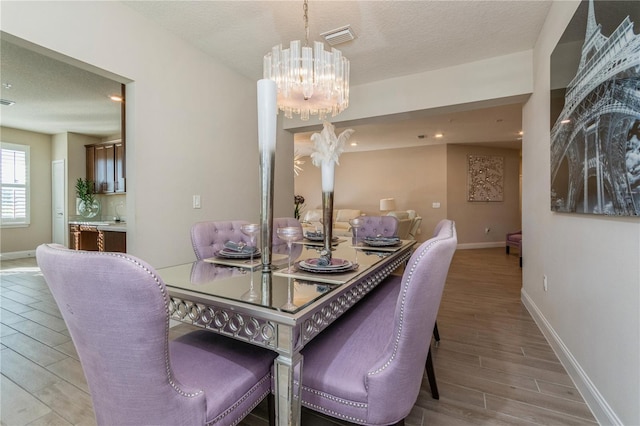 dining area with baseboards, visible vents, a textured ceiling, wood finish floors, and a notable chandelier