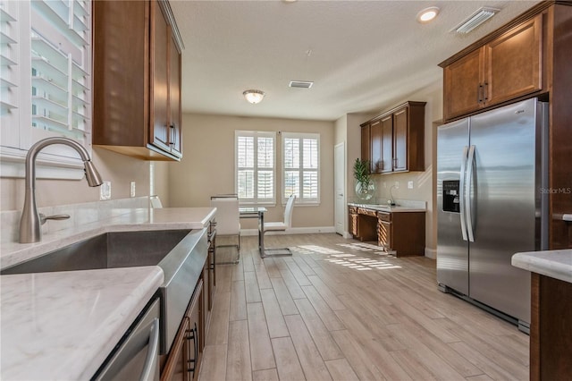 kitchen with stainless steel appliances, visible vents, light wood-style flooring, a sink, and baseboards