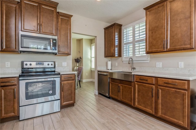 kitchen with stainless steel appliances, light countertops, a sink, and light wood finished floors