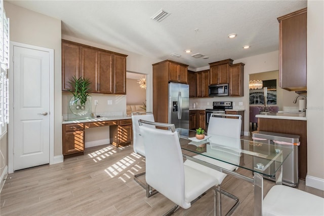 kitchen featuring visible vents, appliances with stainless steel finishes, light wood-style floors, built in desk, and a sink