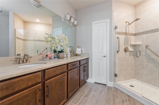 full bathroom with a stall shower, double vanity, a sink, and wood tiled floor