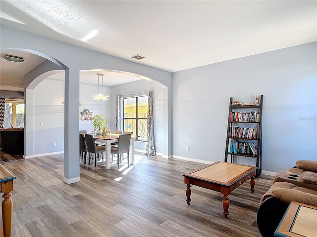 living area with arched walkways, visible vents, and wood finished floors