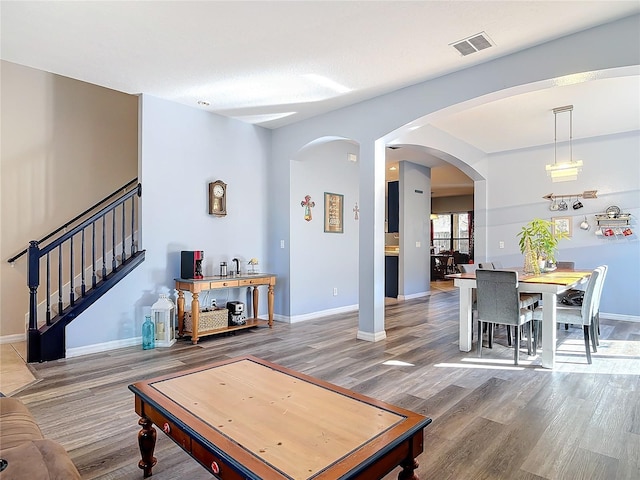 living room featuring visible vents, arched walkways, baseboards, stairway, and wood finished floors