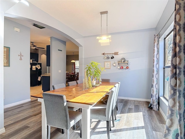 dining space featuring arched walkways, wood finished floors, a ceiling fan, and baseboards