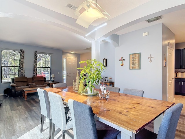 dining area featuring light wood finished floors, visible vents, and arched walkways