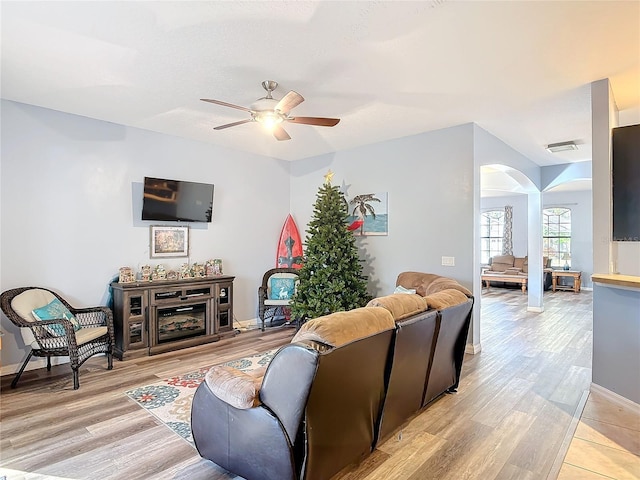 living area with arched walkways, visible vents, a ceiling fan, baseboards, and light wood finished floors